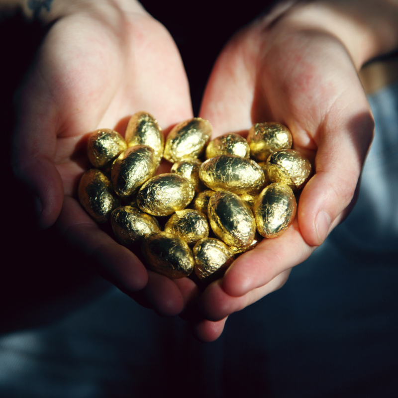 a close up photo of hands together in a cupping motion, hands are filled with gold foiled wrapped candies